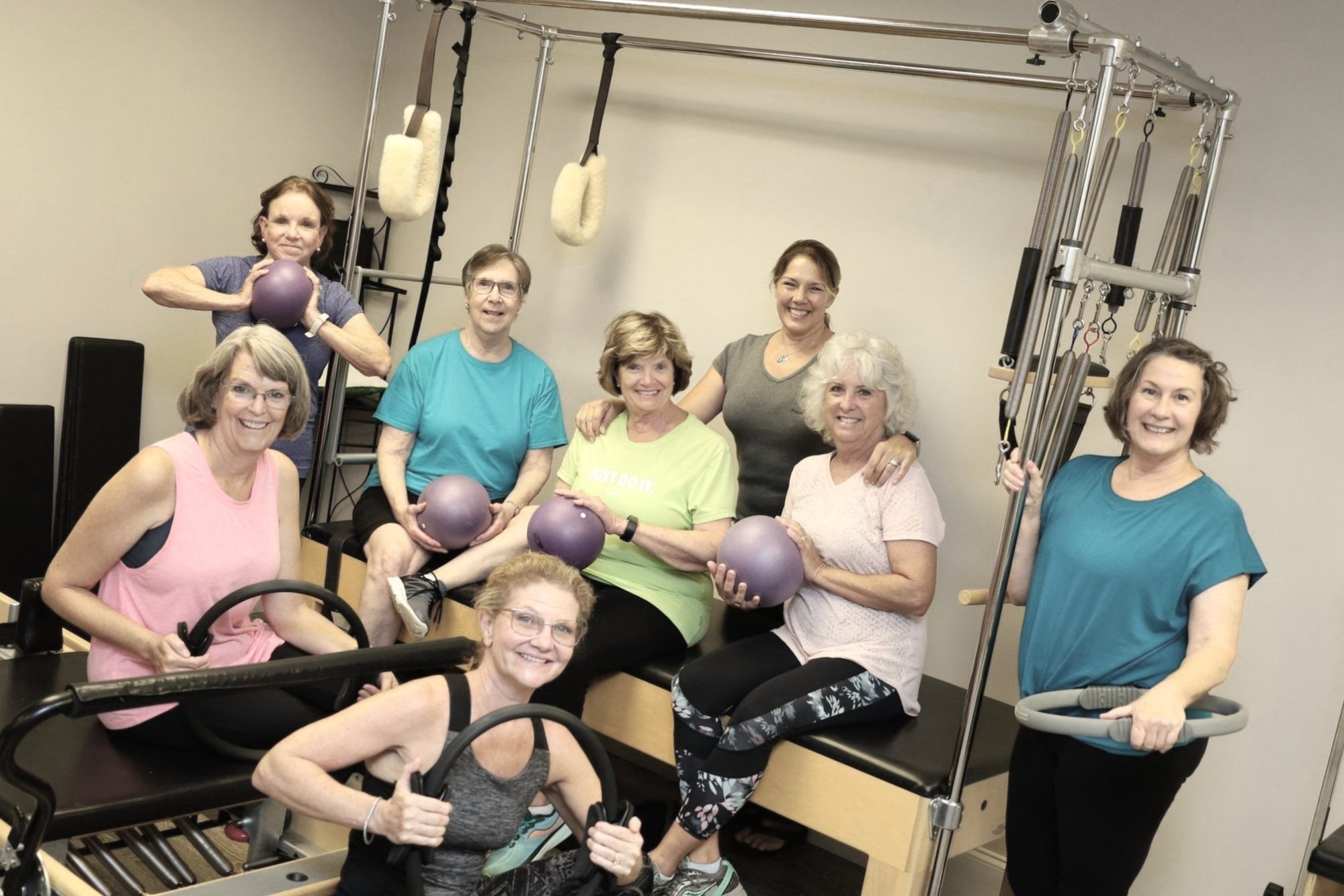 Smiling clients of The Pilates Sanctuary gathered around a Pilates tower and reformers in the studio