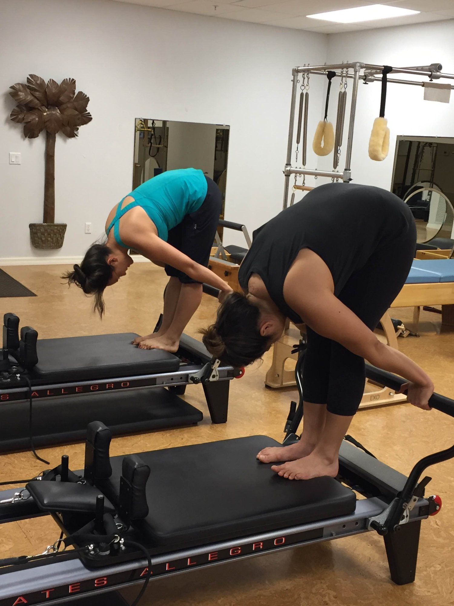 Two clients folding forward over a reformer during a class